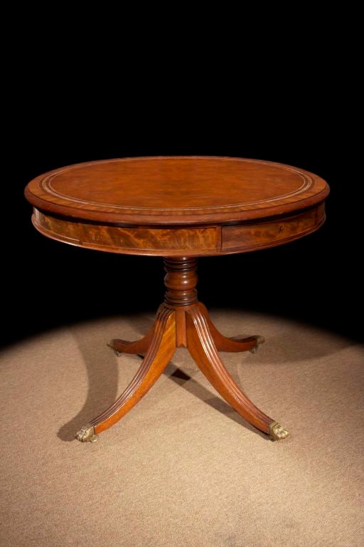 #W052 - Regency mahogany drum table having circular top with tooled leather surface. The apron is set with alternating dummy drawers raised on a turned column on reeded downswept legs, terminating in paw castors,
English, circa 1815

See similar