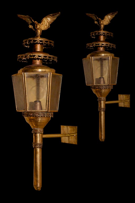 PAIR English brass coach lanterns surmounted by spread wing eagles on tiered top smoke shield and hexagonal working compartment supported by openwork swag and tassel decorated torch handle.<br />
<br />
<br />
See similar examples of coach