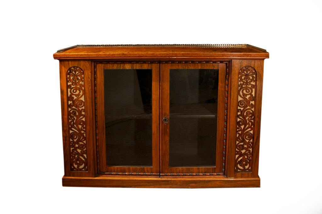 # W516 - Victorian rosewood and amboyna side cabinet surmounted with pierced brass three quarter gallery above a pair of bead-and-reel molded, glazed and panelled doors flanked by pierced arched fret-carved panels, resting on a plinth base.
The