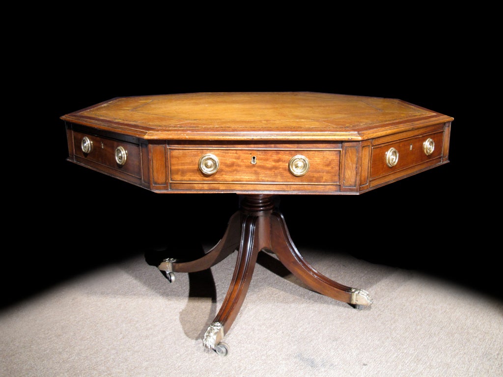 # V143 - Regency style mahogany  rent/drum table with gilt-tooled leather octagonal top surface over frieze with four drawers and four false drawers over bulbous column leading to downswept legs on brass cups and and casters.
English 19th C

See