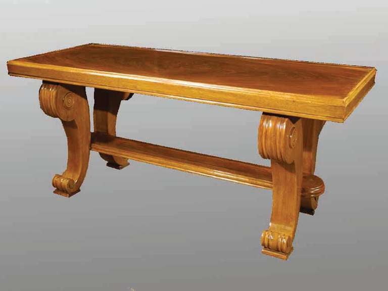 # M050 - Reproduction Art Deco style walnut veneered coffee table. The richly figured burl walnut rectangular top surrounded by a raised edge and all raised on a pair of scrolled legs connected by a flat stretcher.
The geometric stylization of