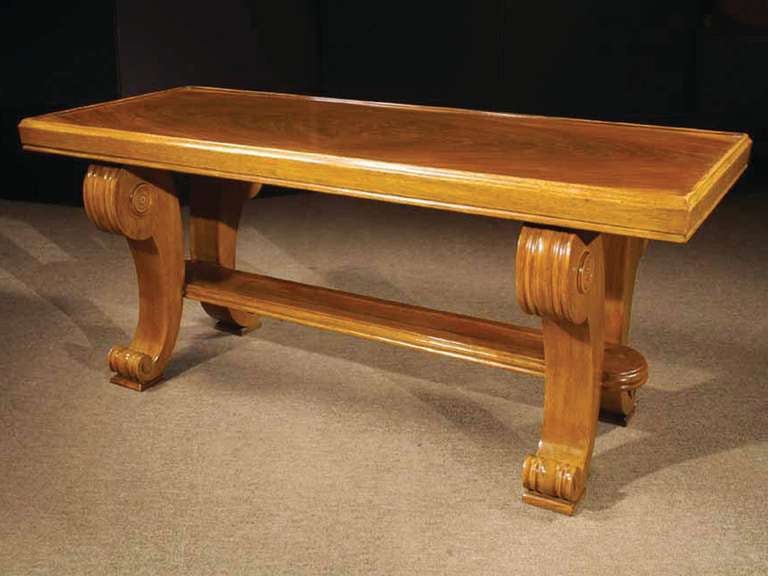 # Y032 - Reproduction Art Deco style walnut veneered coffee table. The richly figured burl walnut rectangular top surrounded by a raised edge and all raised on a pair of scrolled legs connected by a flat stretcher.
The geometric stylization of
