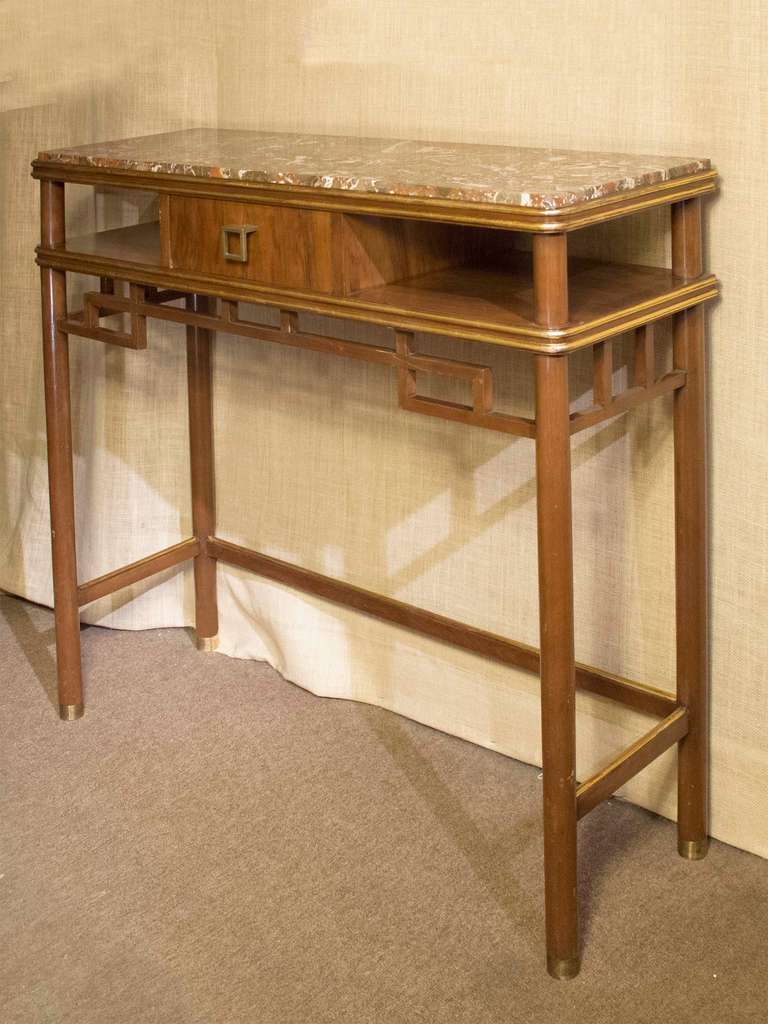 # A1032 - Attractive Mid-Century console table in the modernist oriental style of James Mont. Executed in mahogany with gilt enrichments. The rectangular marble top inset within a double gilt molding repeated in the frieze which centers a single