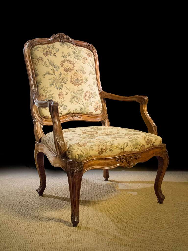 # A1046-Louis XV Rococo carved walnut fauteuil of generous scale and comfortable proportions. The graceful shaped molded back enriched with carved leaf motifs framing the upholstered back. The outward scrolled arms echo the curvaceous shape of the