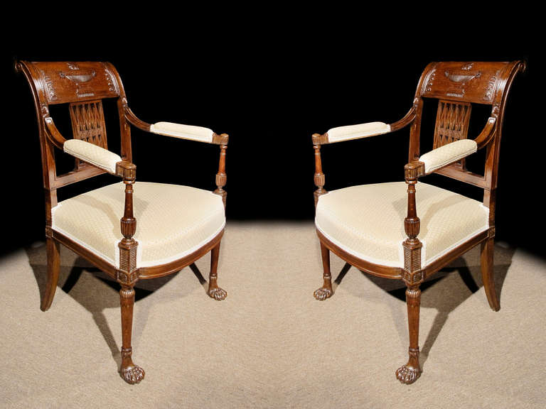 #ZA1055, Pair of Directoire mahogany stained beechwood armchairs with crisply carved neoclassical details. The bold curved crest rail centers an urn above pierced “X” lattice backs with carved rosettes. The pad upholstered arm supported on tapering