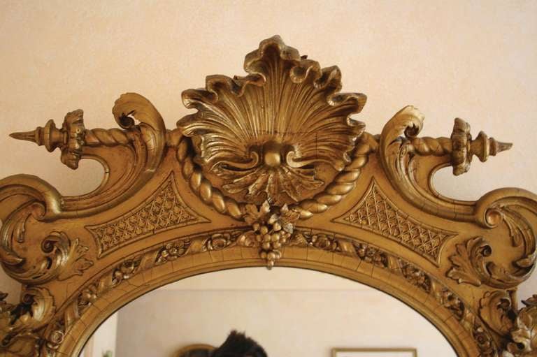 # T068 - American Victorian carved and giltwood hall mirror having a large central mirrored glass with a half round shaped top and all surrounded by a series of carved moldings surmounted by a pediment centering a shell followed by carved flowers
