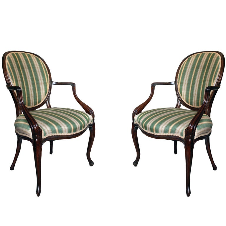 # T079 - PAIR George III style armchairs in the neoclassical taste inspired by Robert Adam. The oval upholstered backs with a molded show frame flanked by down swept arms flanking an upholstered seat above a serpentine shaped apron and raised on