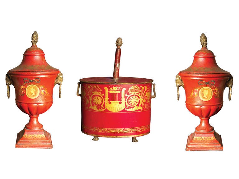 # S085 - Pair of Regency red tole covered urns and flower holder with gilt decoration. The reeded campani-form bowl with gilt cameo roundels and bow-knotted floral garlands, flanked by gilt ram's head ring drop handles. The oval flower holder