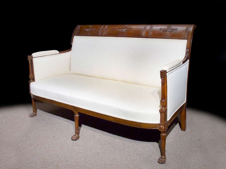 # V098 - Directoire mahogany stained beechwood settee with wide curved crest rails centering carved urns. The upholstered back, seat, and arms, all raised on round tapering legs ending hairy paw feet.
The neoclassical form embodies the simple