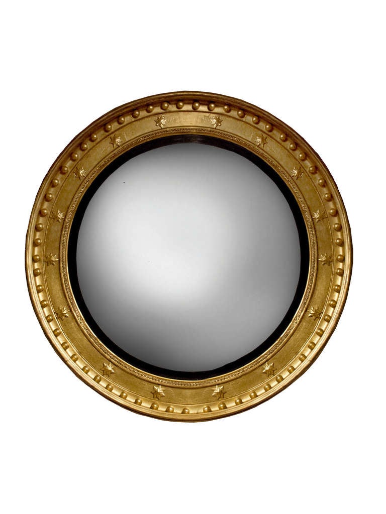 Boldly scaled Regency giltwood convex mirror. The large circular mirror plate surrounded by an ebonized filet molding surrounded by a frieze with applied stars. The molded and reeded frame also has a row of gilt balls. It is unusual to find such a