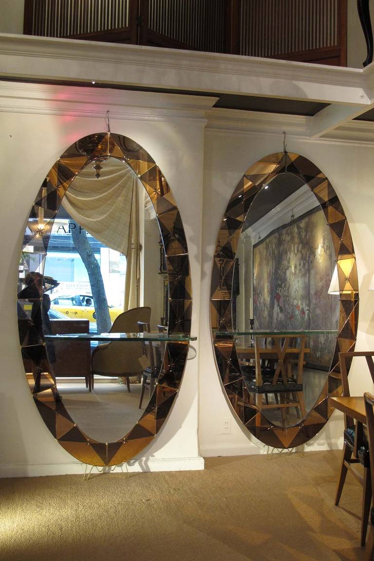 # ZA622. Pair of Mid-Century oval mirrors in the style of Fontana Arte. The border is decorated with a harlequin pattern of triangular shapes in warm colors of brown and tan centering an etched star pattern all resting on shaped brass feet. From the