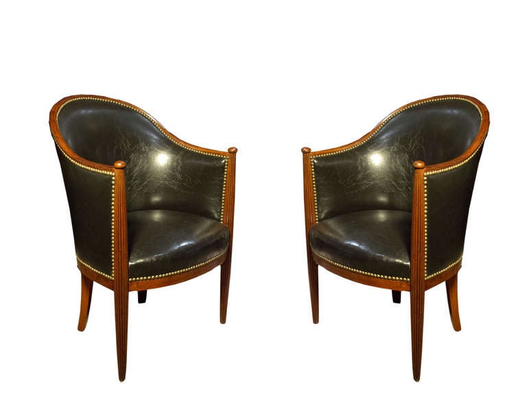 # Y050 - Pair Ruhlmann inspired barrel back bergere chairs executed in mahogany. Note the superb sculptural shape of the frame with it's graceful curved crest rail meeting the molded arm with reeded carving running down the round tapering legs. The