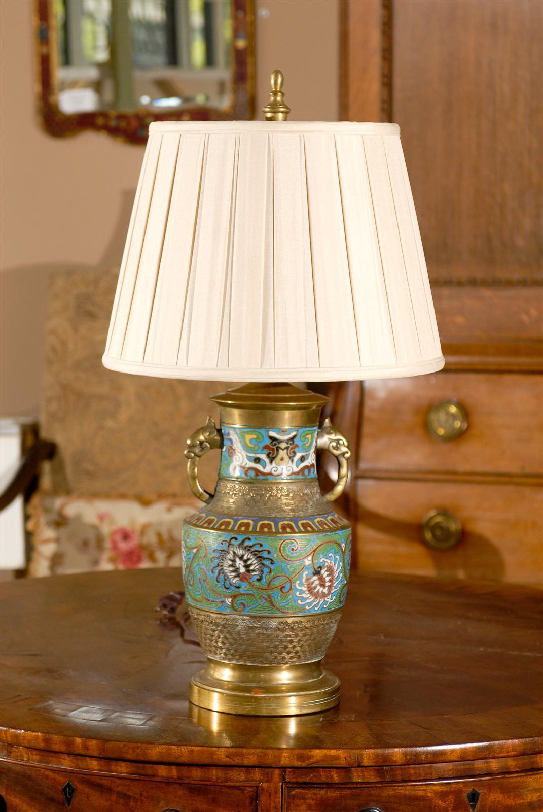 A beautiful cloisonne lamp with turquoise, green and yellow. The base and handles are brass.The ivory pleated shade is new .