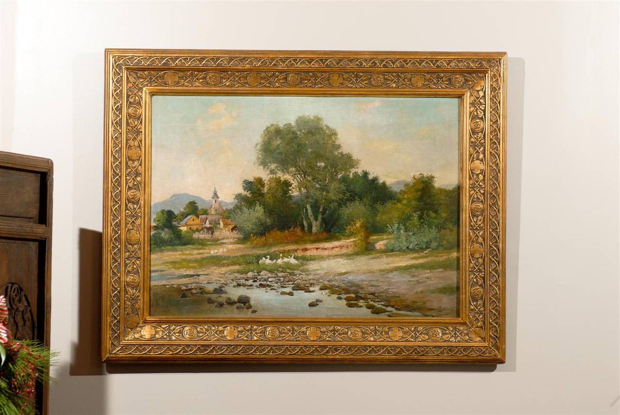 This country landscape has a river and ducks in the forefront. Plus a village with mountains in the distance. Beautifully carved, guilt frame. Excellent condition. An 