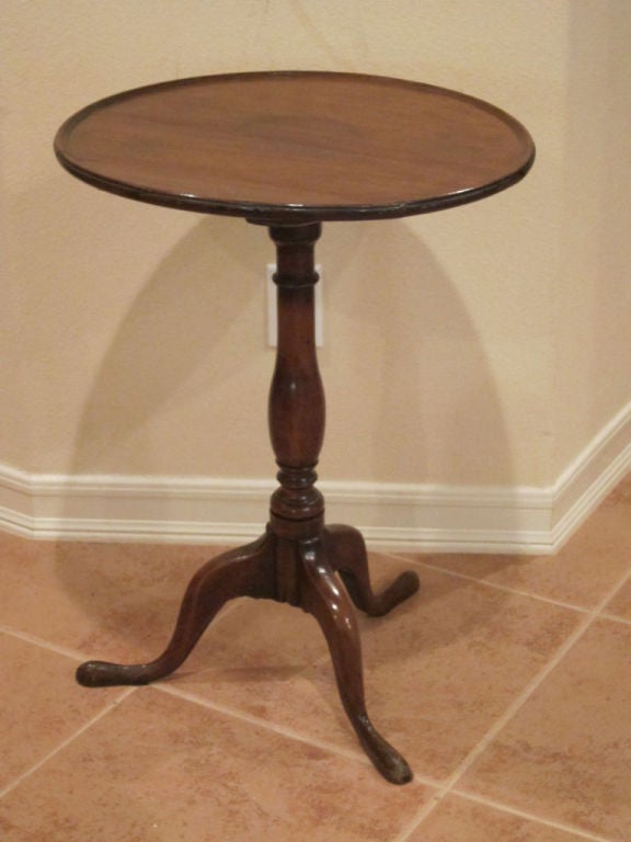 An early English mahogany candlestand with a single board top, molded edge, bulbous column, and splayed tripod legs with slipper feet.  The table has the original finish; however, the latch appears to be a later replacement.  One foot appears to