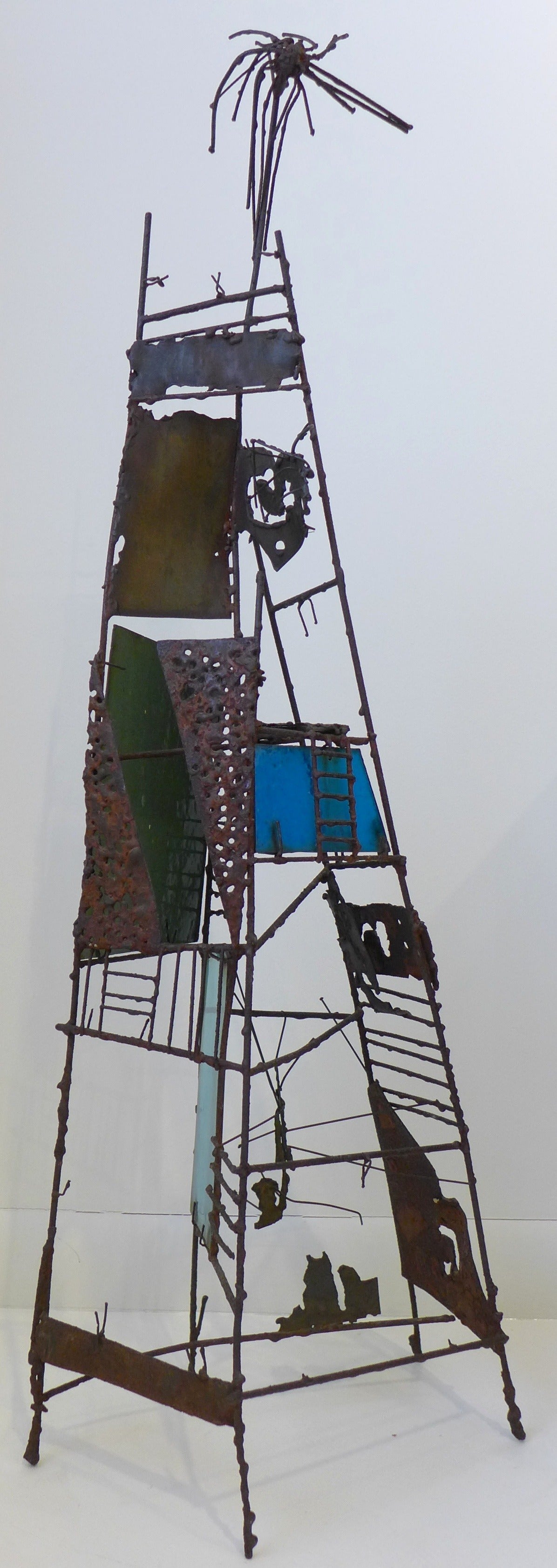 Tall, abstract sculpture of torch-cut, soldered and patinated metal and metal wire, with multicolor glass panels. In the style of Paul Evans, executed circa 1950s.