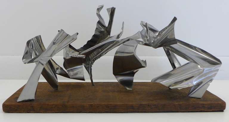 Rhythmic, abstract sculpture cut, bent, and crimped out of one sheet of steel, on its original redwood base.  By Bay Area artist, architect, and jazz musician John Chase Lewis (1924-2013). Signed and dated 1975.  Early in his career, Lewis worked