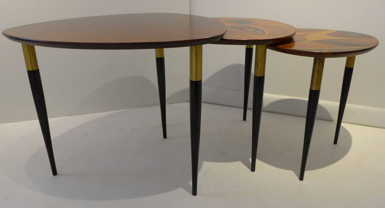 Nest of three cam-shaped tables, one in mahogany veneer, two with boldly abstract exotic wood inlays, all with demountable lacquered wooden legs with brass caps. Made in Sweden, circa 1953, for Erno Fabry Associates of New York City. In remarkably