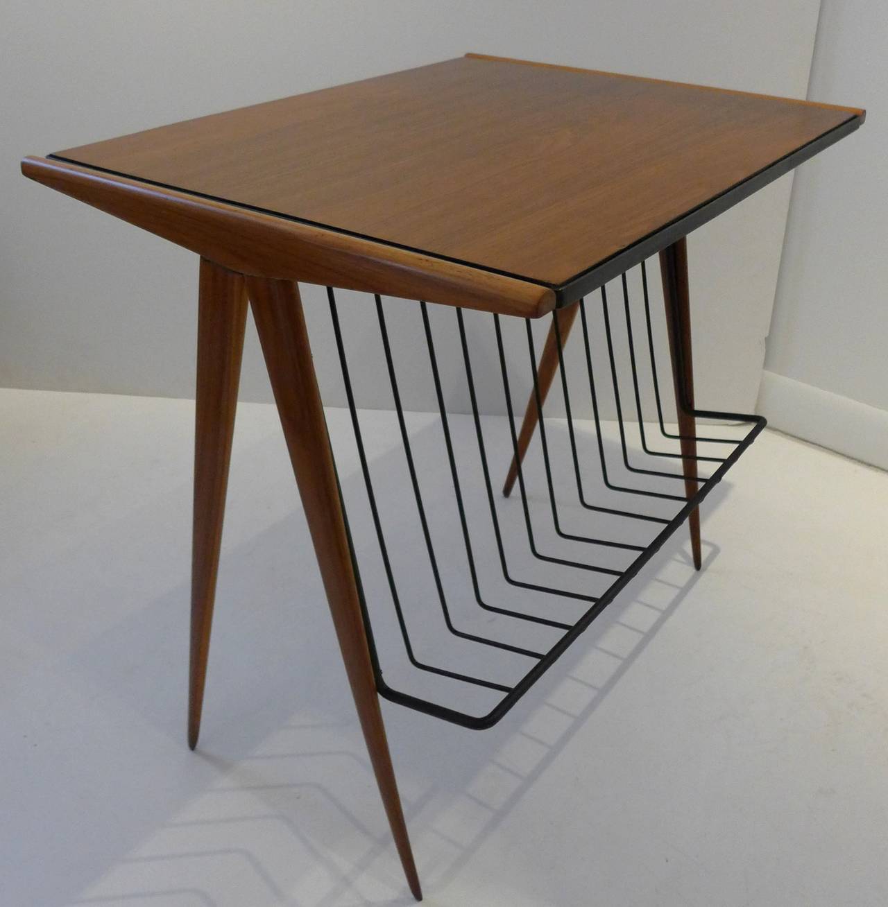 A seldom-seen Mid-Century magazine table in walnut by Arthur Umanoff. The wrought iron magazine holder extends into a border around the top, to which is fastened the compass legs. Manufactured by Post Modern Ltd, circa 1954 for distribution by The