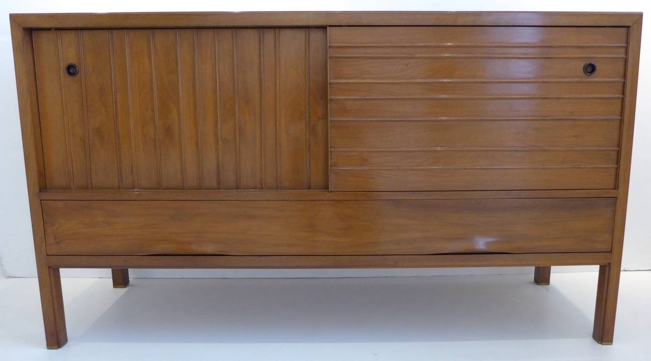 Sideboard of walnut with brass sabots, with contrasting vertical and horizontal battens across the sliding doors and molded plywood finger pulls along the bottom drawer, a technically challenging flourish unique to Dunbar. With subtle accents of