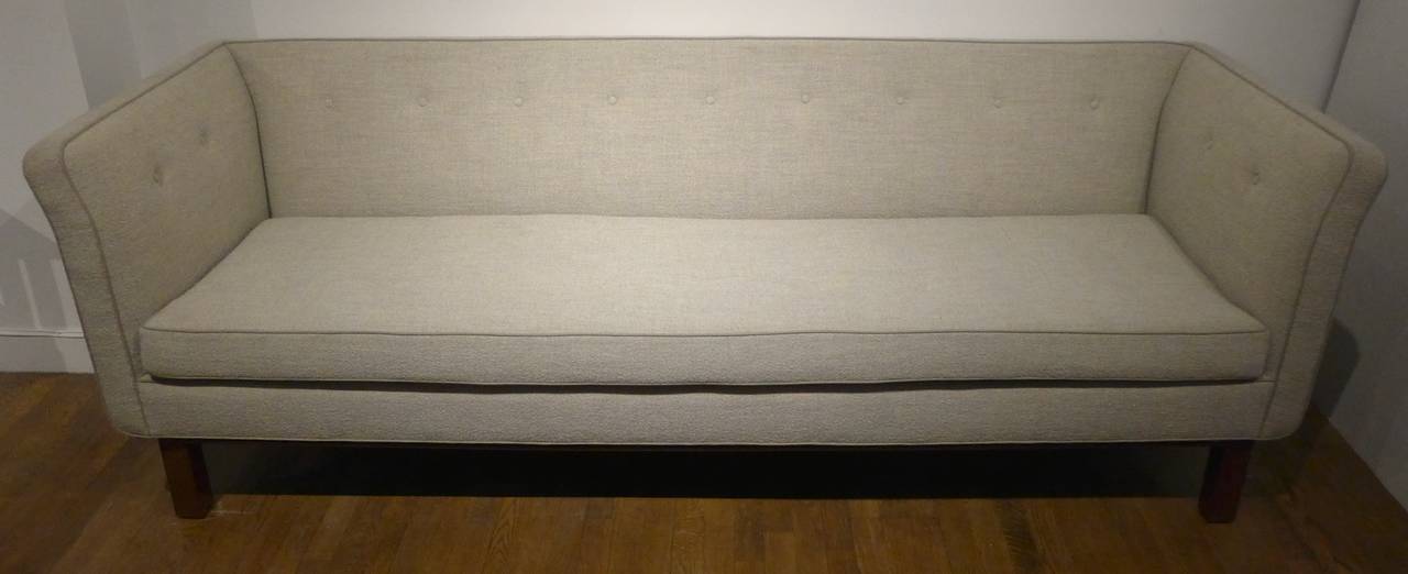 An elegant, comfortable and generously proportioned even-arm sofa with a mahogany base. Reupholstered in a heather gray fabric with greige piping. A hard-to-find and sophisticated 1947 Edward Wormley design, produced by Dunbar Furniture.