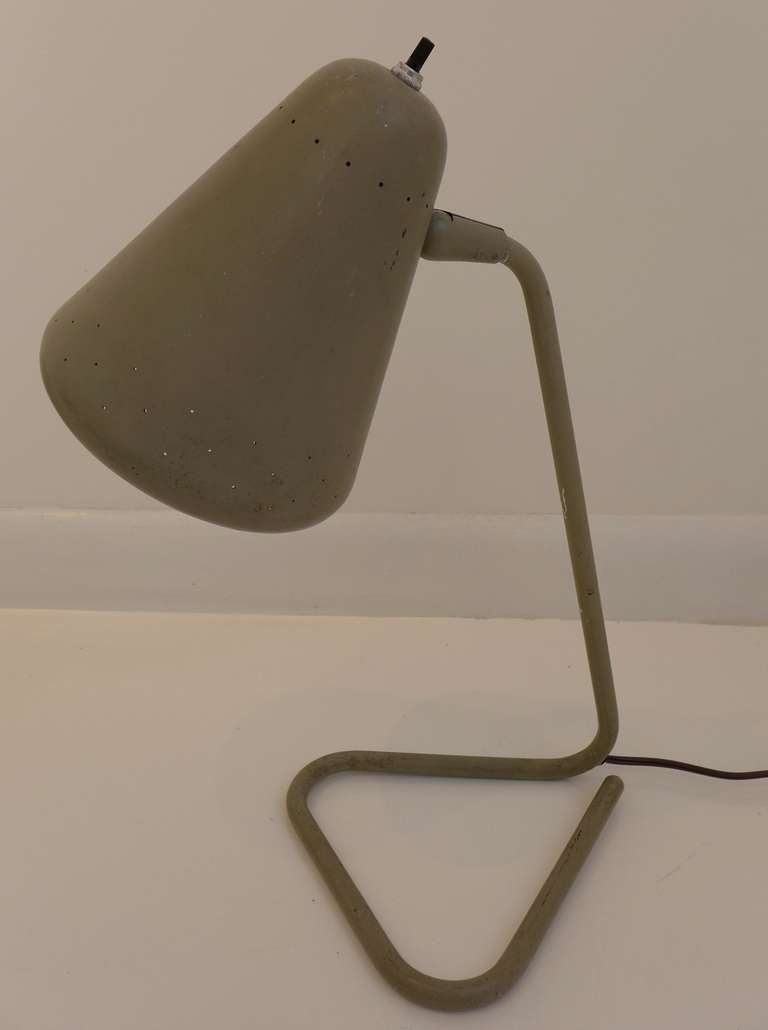 Table or desk lamp with pivoting reflector, model no. 4460, by Kurt Versen Lamps of Englewood, NJ.  In original sage green baked enamel paint, with expected areas of loss on stem. Reflector is perforated for both decorative and ventilation reasons.