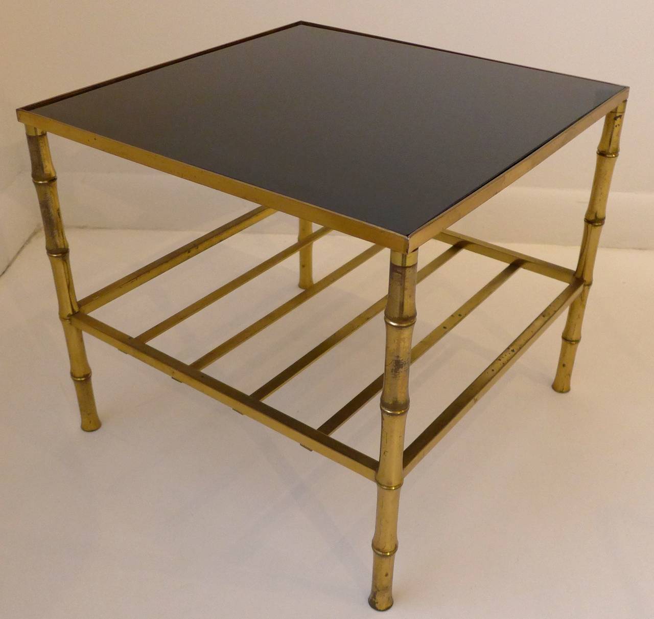 Side table of solid brass with faux bamboo legs, an open medial shelf and a black vitrolite top. Probably French, 1950s. In the style of Maison Bagues. In fine original condition, with expected wear to the metal and light scratching to the glass,