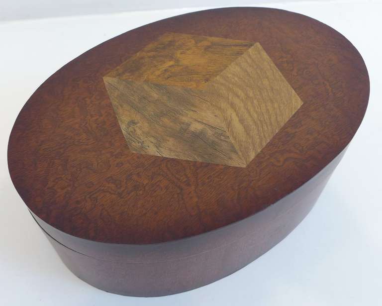 Oval box of stained tiger maple with a multi-wood veneer marquetry cube motif on the lid. Interior is lined in red velvet, top and bottom.  American, circa 1940s.  In the style of Andrew Szoeke.