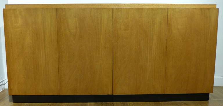 Sideboard or cabinet (model #5222A) of bleached mahogany with piano-hinged doors, designed by Edward Wormley and produced by Dunbar Furniture. The interior is fitted with six sliding tray drawers on either side, flanking a space with a pull-out