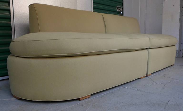 Moderne sofa composed of two mirrored units with floating backs, curved sides, and wooden chock feet. In the style of Modernage, circa 1930s. The present fabric is structurally fine, but has a few areas of discoloration, notably a circular mark on