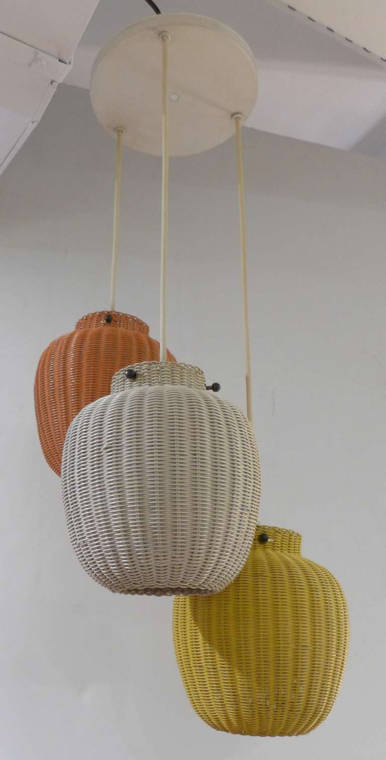 Scandinavian hanging fixture with three woven wicker globes in yellow, coral, and white.  Nicely machined brass fittings. The three globes suspend from a single canopy, and can be adjusted in height. An unusual mid-century item, in remarkably good