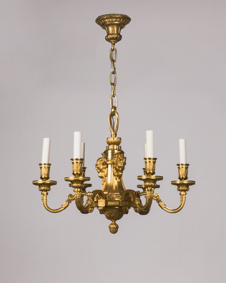 AHL3731
A very nicely chased antique six light chandelier in bronze with its original gilded finish. The rectangular-section arms spring off a body detailed with ram heads and support foliate cups and wax pans.

Dimensions:
Current height: