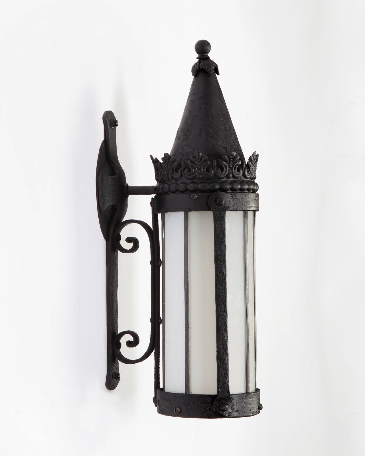 AEX0581

Circa 1920
A pair of wrought iron exterior wall lanterns with cylindrical leaded opaline glass shades, in their original weathered black paint finish. Due to the antique nature of this fixture, there may be some nicks or imperfections in