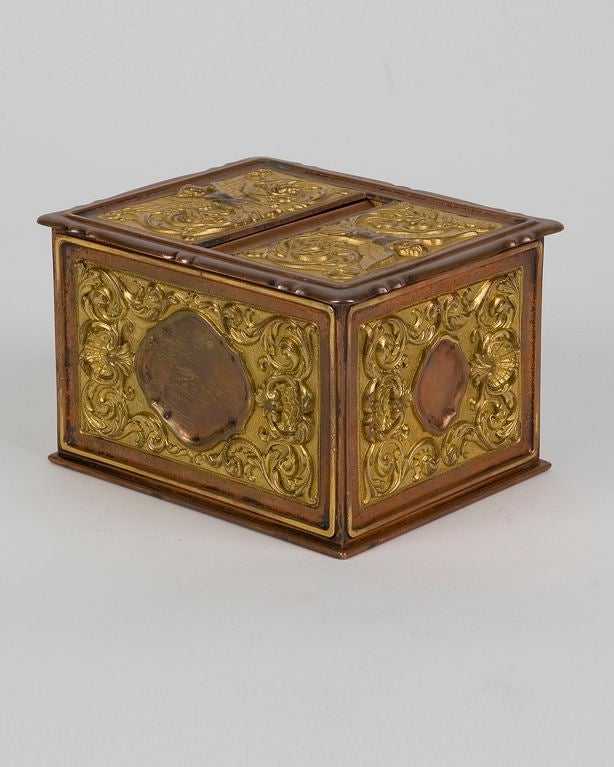 ATA1389
A beautiful, finely-detailed copper and gilt brass cigarette box. The action of lifting the lid cleverly places a cigarette on the small middle recess when it is reset. The top is detailed with facing female angels. Signed by the New York