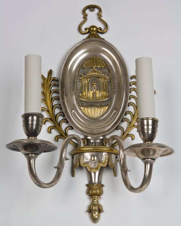 AIS2756
A pair of antique double-light sconces in their original two tone aged nickel and brass finish. The central image of the backplate is a tempietto framing a classically robed figure. The arms spring from an aproned arm receiver plate. Signed