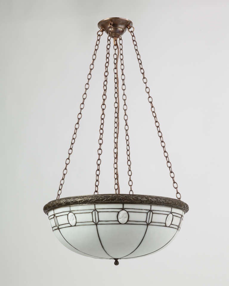 AHL3771

An antique inverted dome chandelier with leaded opalescent glass accented by cameos. The lens is bordered in laurel banding; the metalwork in its original darkened finish. Due to the antique nature of this fixture, there may be some nicks