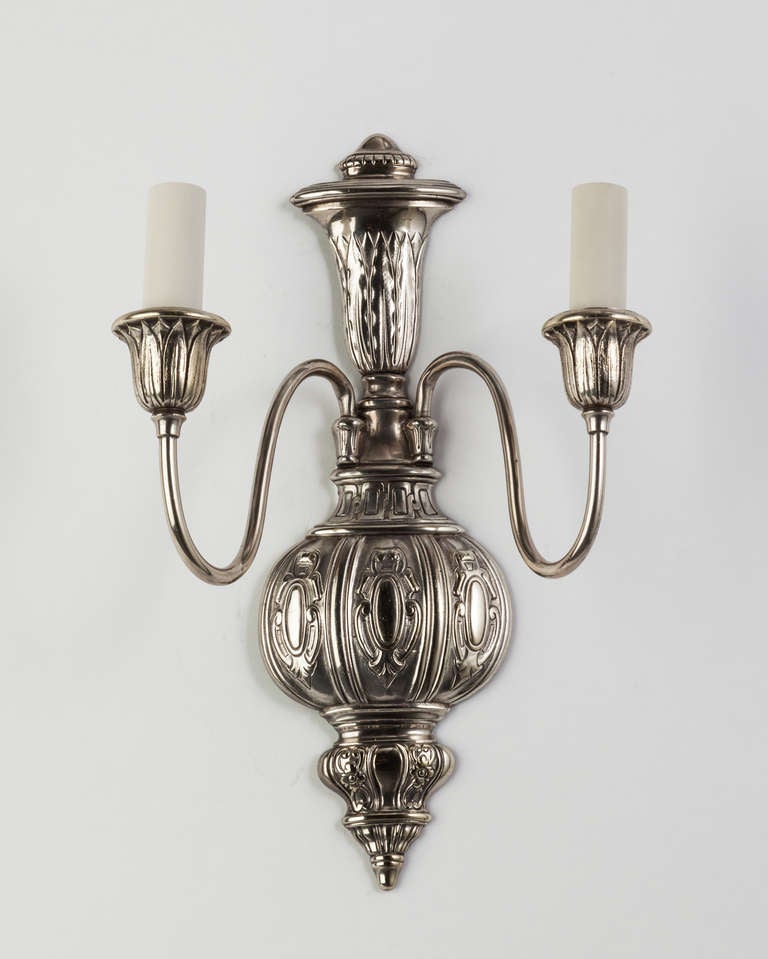 AIS2870
Coppia di appliques a due bracci in silverplate e bronzo fuso. Le piastre posteriori sono intagliate a basso rilievo con cartigli e dettagli fogliacei; le coppe sono avvolte da un motivo di foglie e dardi. Circa anni '20.

Dimensioni:
In