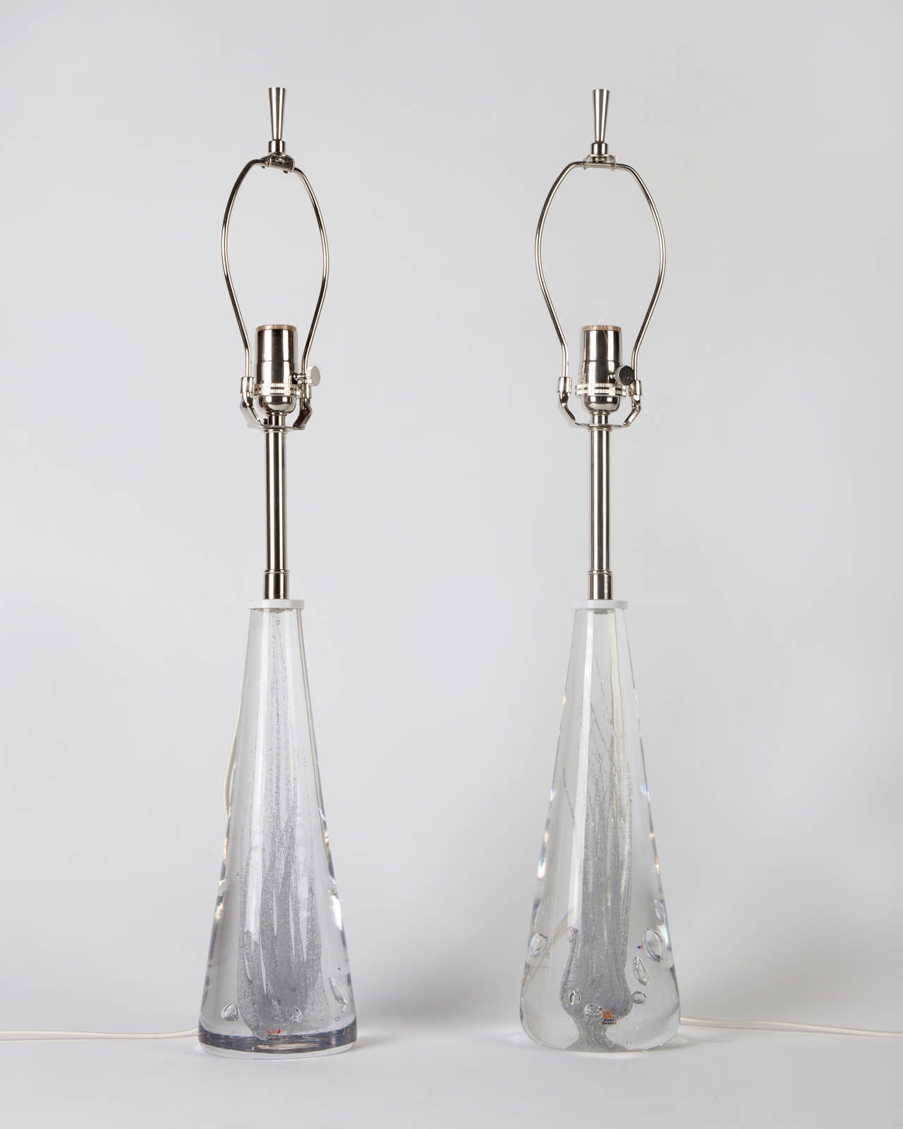 ATL1887

A pair of solid glass lamps having centers of swirled air bubbles. Topped with nickel fittings. Signed by Vicke Lindstrand for the Swedish maker Kosta. Due to the antique nature of this fixture, there may be some nicks or imperfections in