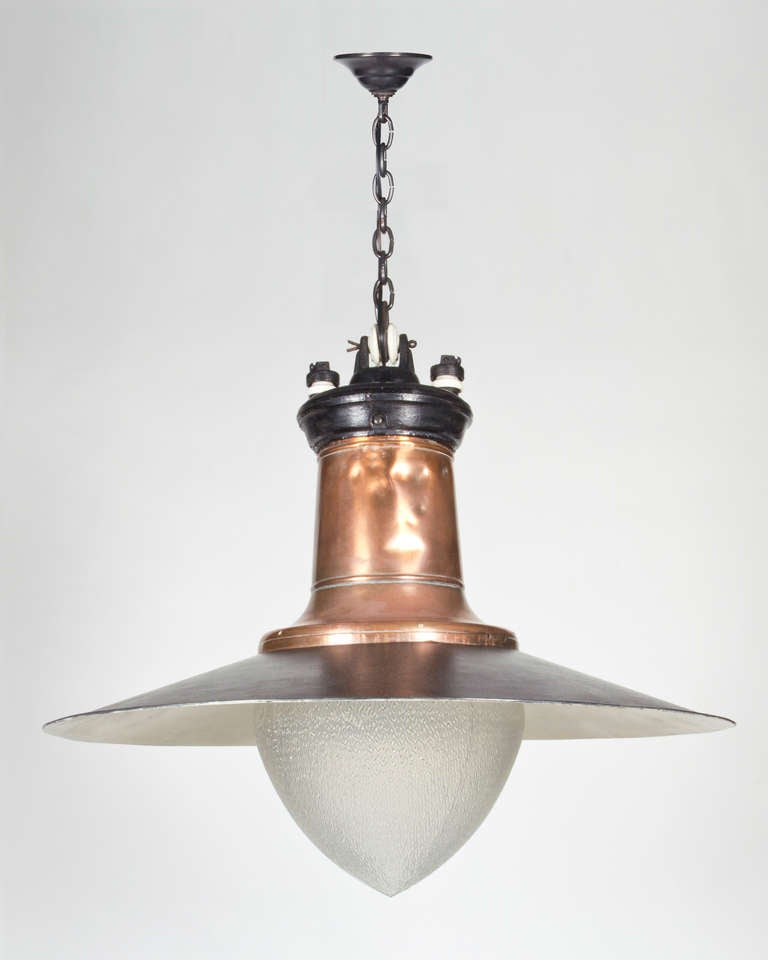 Ancienne lanterne de gare en arc carbone avec un abat-jour en verre opalin texturé sous un large bouclier en acier émaillé noir:: surmonté d'un capot en cuivre. Signé par le fabricant General Electric Co. En raison de la nature antique de ce