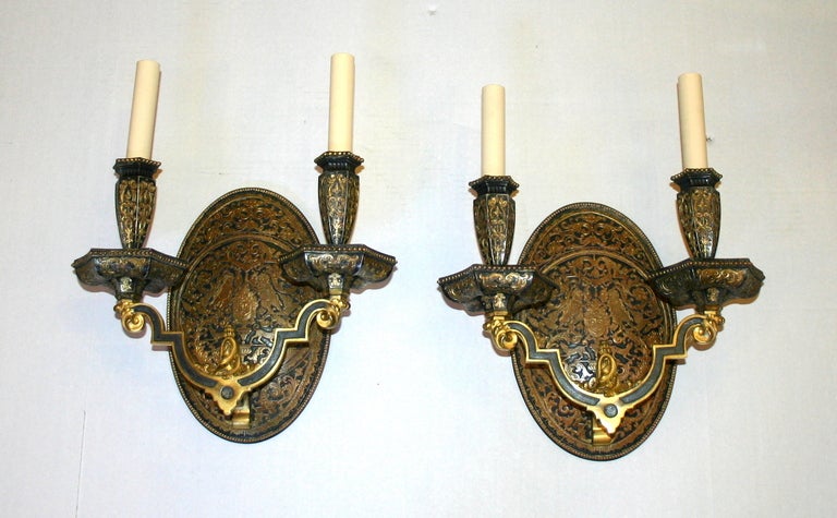 A pair of neo classic style double light gilt and dark patina sconces with original finish.  Oval backplate with stylized foliage and arabesques, hounds and putti.