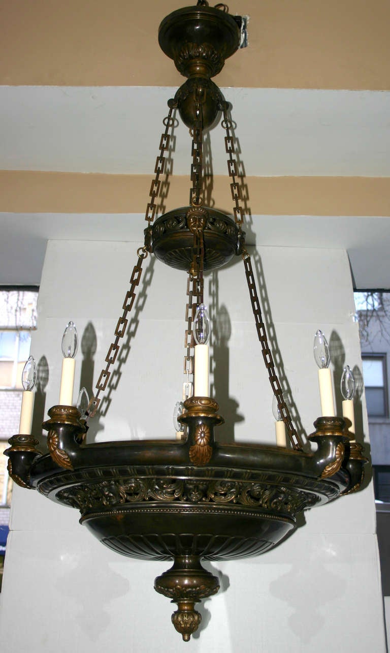 A circa 1920 bronze neoclassic style American chandelier with masks details on body, open work motif and rectangular chain. Eight lights.
Measures: 47