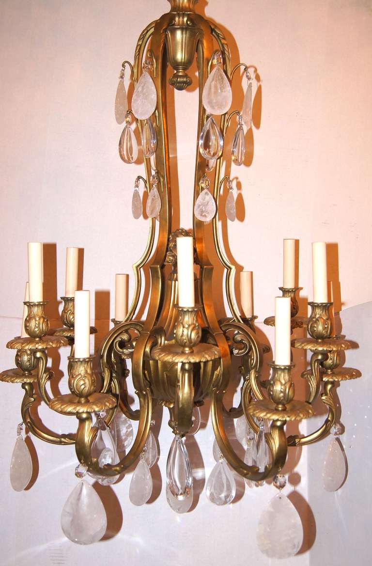 Zwölfarmiger, zweigeschossiger Kronleuchter aus vergoldeter Bronze im französischen Neoklassizismus um 1900 mit Bergkristall-Anhängern.

Abmessungen:
Mindesthöhe: 42