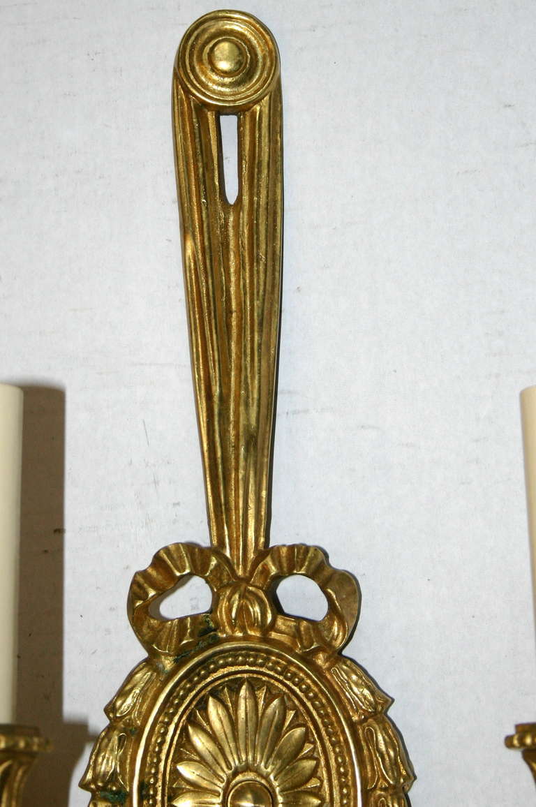 Ein Paar vergoldete Bronzeleuchten im neoklassischen Stil von Caldwell mit doppeltem Arm und ovaler Rückplatte mit Rosette. Verkauft in Paaren. Der Preis gilt pro Paar. 

Maße: Höhe 18,5 in.
Tiefe 5,5 Zoll.