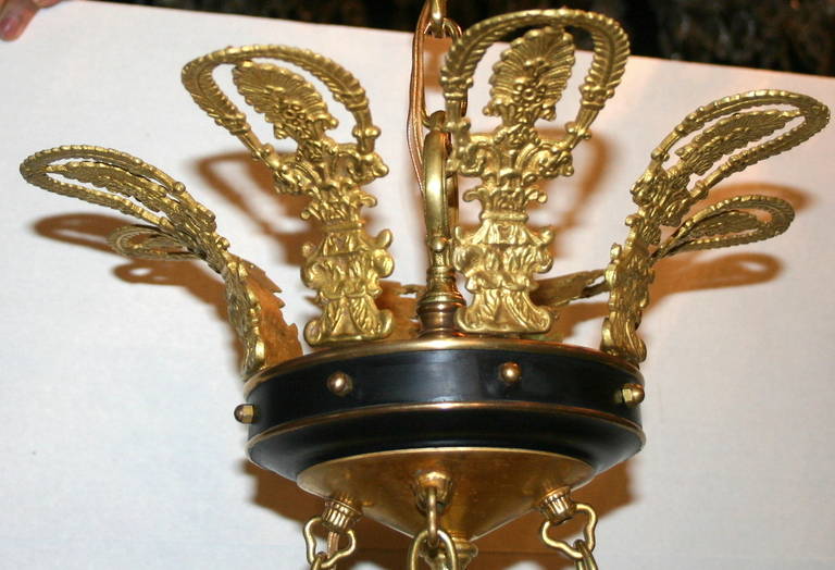 Ein achtflammiger Kronleuchter aus vergoldeter Bronze und Zinn aus den 1920er Jahren im Empire-Stil. Der Korpus mit Medaillonverzierung und Kette mit Kristalleinsätzen.

Abmessungen:
33