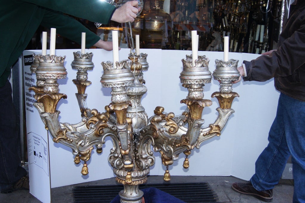 A French carved and silver leaf wooden chandelier with gilt details, scrolling motif on arms and body and gilt tassels on arms.

Measurements:
Diameter 46