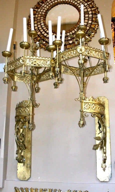 Pair of Italian, early 1900s, gilt iron torchieres of gothic design, seven lights each. These monumental iron sconces have an open work body and foliage motif on arms. The arms support a seven light candelabra each. They have been mounted on