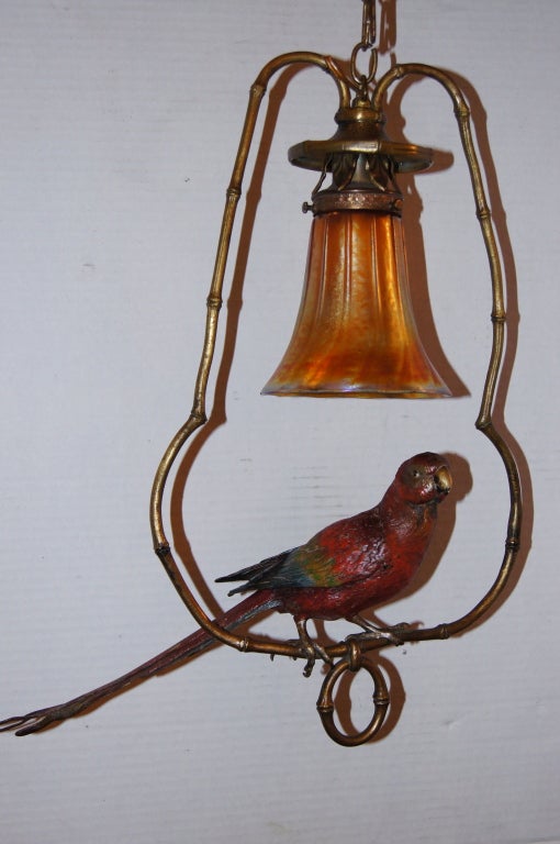A painted and patinated bronze light fixture, with iridescent glass shade. The body of the fixture shaped as a bamboo ring and with a painted parrot at center. Single light.
20