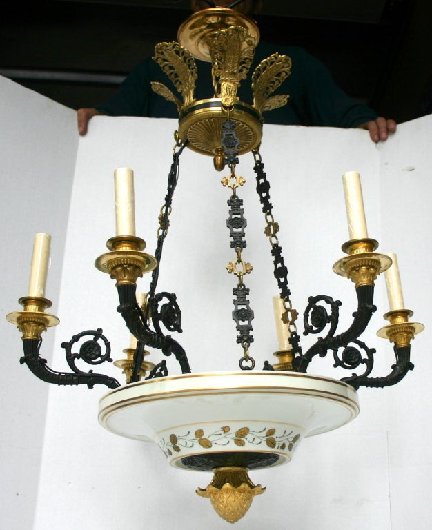 A six-arm Empire style chandelier with white porcelain body with gilt foliage motif decoration and patinated and gilt arms and chain.

Measurements:
Height: 30