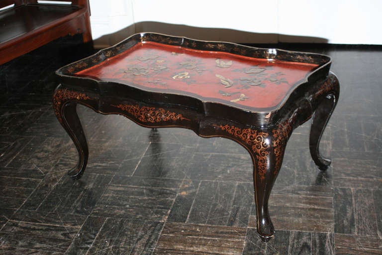 Mid-20th century black lacquer and gold decorated cocktail table with red and black removable chinoiserie tray top, cabriole legs slipper feet.