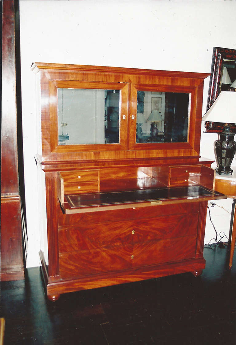 19th century mahogany secretaire or commode, the upper section set back with molded cornice above a pair of mirrored doors, three long drawers below flanked by fluted sides supported by bun feet.